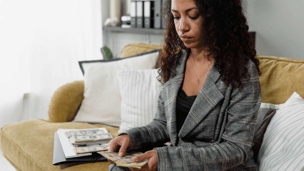 Woman sitting on a couch in the study balancing money indicating financial independence and management.